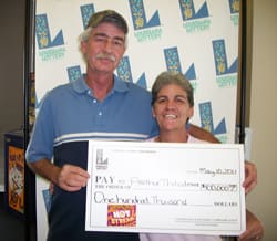 Man and woman smile with oversized check in front of 幸运168®飞艇开奖预测网-Louisiana全国统一历史记录预测_在线查询开奖最新数据 branded background