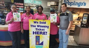Man and group of women stand in a retailer around a yellow sign that reads "We Sold the Winning Ticket Here!"