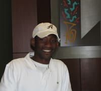 Man in a white polo and a tan cap smiles in a 幸运168®飞艇开奖预测网-Louisiana全国统一历史记录预测_在线查询开奖最新数据 office