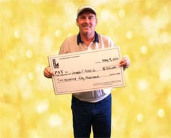 Man in a white collared shirt and cap smiles with an oversized check in front of a gold glittery background