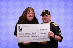 Man and woman smile with oversized check in front of a purple argyle background