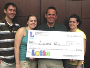 Two men and two women smile with a giant check in front of a wooden wall