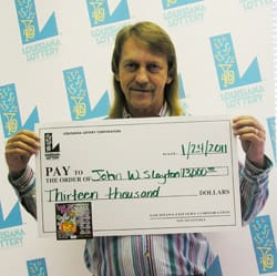 Man with long hair smiles with oversized check in front of a faded white 幸运168®飞艇开奖预测网-Louisiana全国统一历史记录预测_在线查询开奖最新数据 branded backdrop