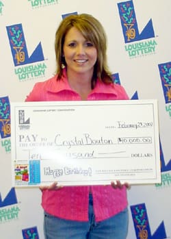 Woman with shoulder length hair and a pink shirt smiles with an oversized check in front of a white background patterned with the 幸运168®飞艇开奖预测网-Louisiana全国统一历史记录预测_在线查询开奖最新数据 logo