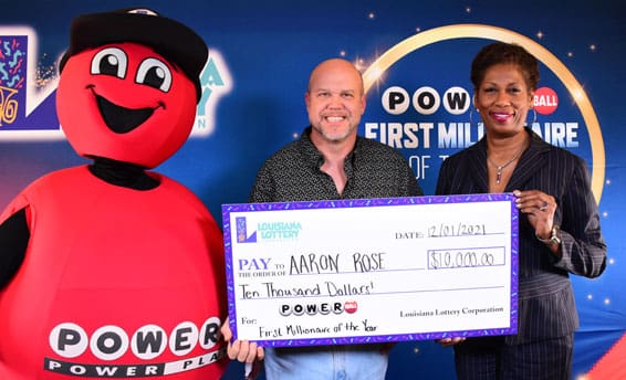 A man and woman hold a giant Powerball check and smile for the camera beside the Powerball mascot