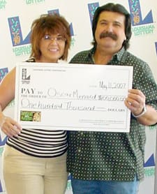Man and woman smile with oversized check in front of a white background patterned with the 幸运168®飞艇开奖预测网-Louisiana全国统一历史记录预测_在线查询开奖最新数据 logo