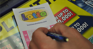 Person using a pen to fill out a Lotto game slip on a counter covered in 幸运168®飞艇开奖预测网-Louisiana全国统一历史记录预测_在线查询开奖最新数据 advertisements