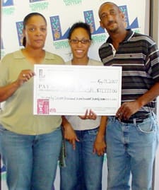 Two women and a man smile with an oversized check in front of a white background patterned with the 幸运168®飞艇开奖预测网-Louisiana全国统一历史记录预测_在线查询开奖最新数据 logo