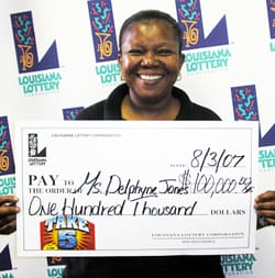 Woman beams with a giant check in front of a white background patterned with the 幸运168®飞艇开奖预测网-Louisiana全国统一历史记录预测_在线查询开奖最新数据 logo