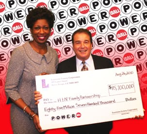 Man and woman smile with oversized check in front of a red and white background branded with the Powerball logo