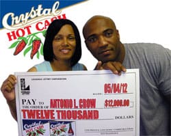 Man and woman pose with oversized check in front of white and blue Crystal Hot Cash branded background