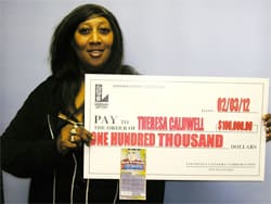 Woman smiles with an oversized check in front of a gray wall