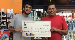 Two men hold a large check from Lotto in front of a register