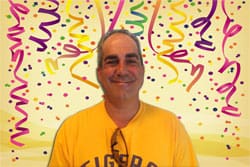 Man in a yellow LSU tshirt smiles in front of a yellow background with animated streamers and confetti