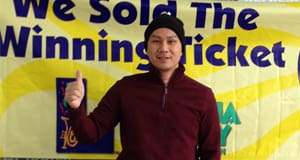 Man holds a thumbs up and smiles in front of a yellow banner that reads "We Sold the Winning Ticket"