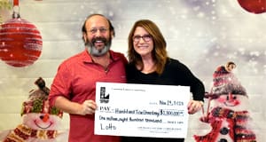Man and woman hold an oversized check from Lotto in front of a winter background
