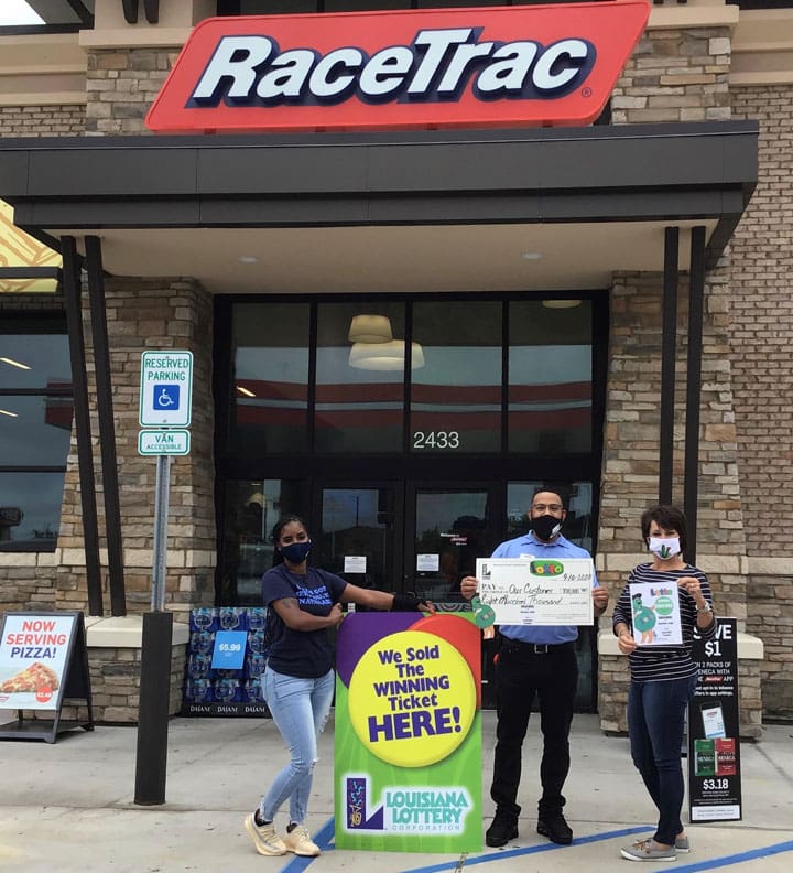 Man with a giant check and two women stand in front of a RaceTrac retailer beside a sign that reads 