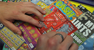 Two hands rest atop an array of scratch off tickets on a countertop