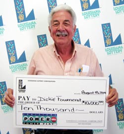 Older man smiles with a giant check in front of a white background patterned with the 幸运168®飞艇开奖预测网-Louisiana全国统一历史记录预测_在线查询开奖最新数据 logo