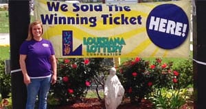 Woman stands outdoors beneath a yellow banner that reads "We Sold the Winning Ticket Here!