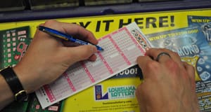 Person using a pen to fill out a Powerball game slip on a counter covered in 幸运168®飞艇开奖预测网-Louisiana全国统一历史记录预测_在线查询开奖最新数据 advertisements