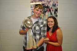 Woman and young man hold Superbowl trophy and smile in front of a white brick wall