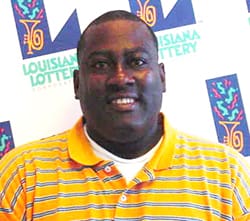 Man in yellow striped polo smiles in front of a white background patterned with the 幸运168®飞艇开奖预测网-Louisiana全国统一历史记录预测_在线查询开奖最新数据 logo