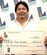 Man in white collared shirt smiles with oversized check in front of a white background patterned with the 幸运168®飞艇开奖预测网-Louisiana全国统一历史记录预测_在线查询开奖最新数据 logo