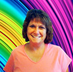 Brunette woman in a pink tshirt smiles in front of a rainbow digital background