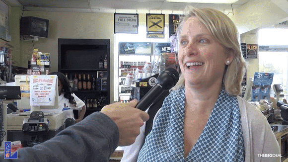 Blonde woman with blue patterned shirt and tan cardigan speaks into a microphone at a retailer