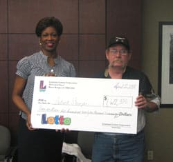 Man an woman hold oversized check in front of a wooden wall
