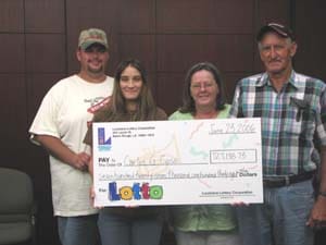 Two men and two women smile with a giant check in front of a wooden wall