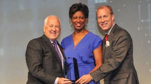Two men and a woman smile with a glass award