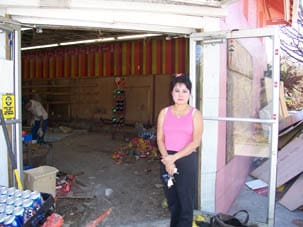 Short haired woman in pink tank top stands in the doorway of a gutted store