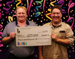 Two men laugh with an oversized check in front of a dark digital background with animated streamers and colorful confetti