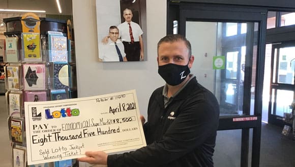 Man in a mask holds a check for $8,500 from Lotto
