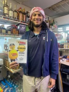 Man in a beanie and blue sweatshirt smiles for the camera and holds a sign that shows how much he won with Mega Millions