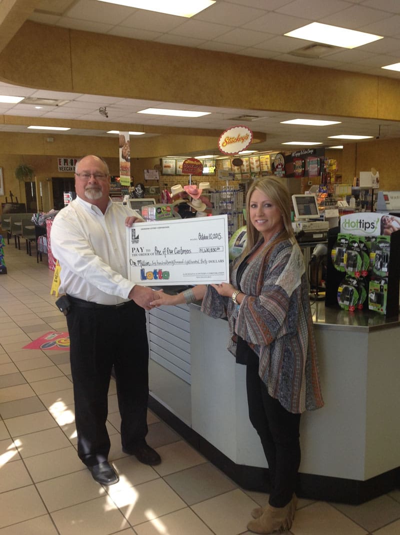 Man and woman stand in a retailer and hold an oversized check while shaking hands.