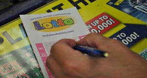 Person using a pen to fill out a Lotto game slip on a counter covered in 幸运168®飞艇开奖预测网-Louisiana全国统一历史记录预测_在线查询开奖最新数据 advertisements