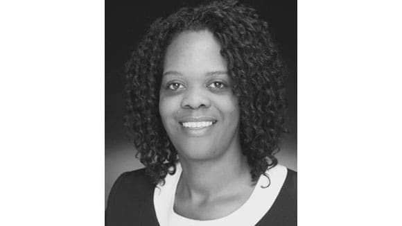 Black and white image of a woman with curly dark hair, white shirt, and black sweater smiling at the camaera