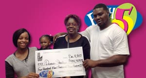 Family poses with an oversized check in front of a pink Easy 5 branded background