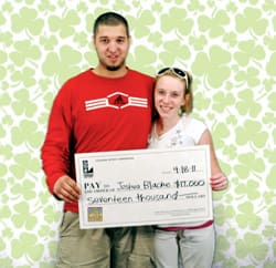 Man and woman smile with oversized check in front of green and white clover background
