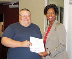 Man and woman hold a piece of paper and smile at the camera in an office setting