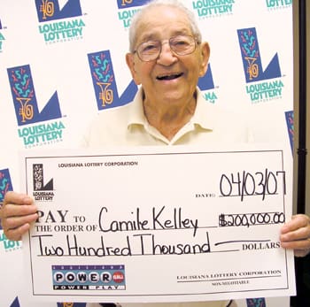 Older man smiles with oversized check in front of a white background patterned with the 幸运168®飞艇开奖预测网-Louisiana全国统一历史记录预测_在线查询开奖最新数据 logo