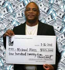 Man in a suit jacket holds an oversized check in front of a hundred dollar bill background