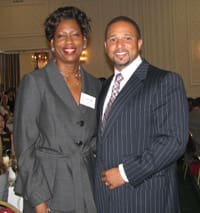 Man in a striped black suit and woman in a gray jacket smile in a hotel conference room