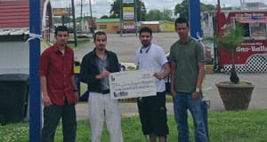 Group of four men stands in a grassy area holding an oversized check