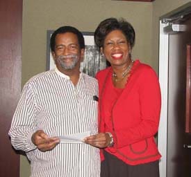 Man and woman hold a normal sized check and smile in an office setting